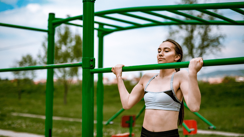 A lady doing a chin up on a bar in a park
